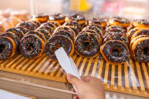Human hand using clamp picking frosted chocolate donut at bakery Stock Photos