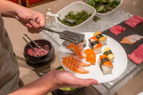 Human hand using tongs picking assorted sushi in buffet restaurant Stock Photos