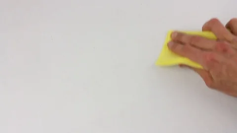 Human hand wipes and cleans the white surface of table with yellow cloth Stockbeeldmateriaal 103188322