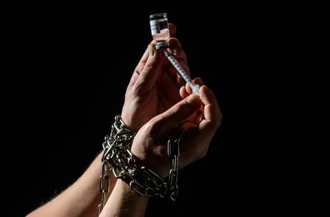 Human hands chained in chains are taking an injection into a syringe from an amp Stock Photos