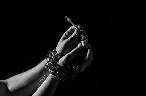 Human hands chained in chains are taking an injection into a syringe from an amp Stock Photos