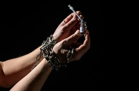 Human hands chained in chains are taking an injection into a syringe from an amp Stock Photos