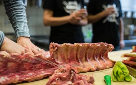 Human hands of chef cutting rack of lamb meat lying on wooden kitchen cutting Stock-Fotos