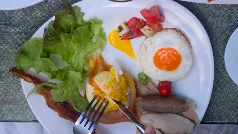 Human hands cut benedict egg with hollandaise sauce with fork and knife. Plate Видео 200897753