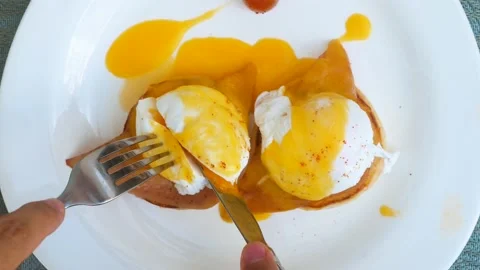 Human hands cutting freshly cooked eggs benedict with hollandaise sauce with Stock Footage 200885816