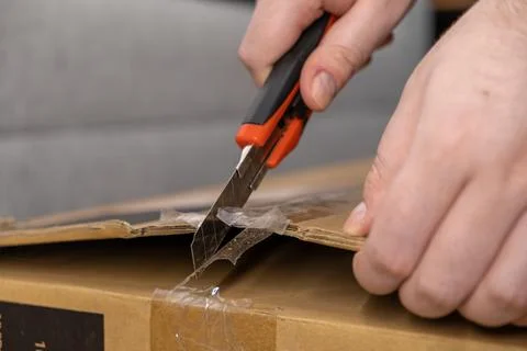 Human hands cutting open a taped brown cardboard shipping box with a sharp .. Stock Photos