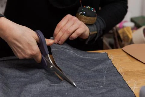 Human hands cutting out the template of fabric with dressmaker shear for maki Stock Photos