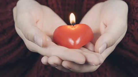 Human hands hold heart shaped burning red candle against red cozy sweather. Y Stock Footage 112718345