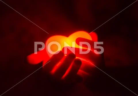 Human hands holding red glowing heart in the dark Stock Photos