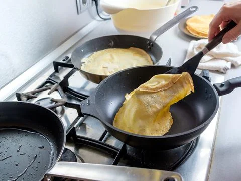 Human hands with a kitchen spatula turn over a hot fragrant pancake in a pan Stock Photos