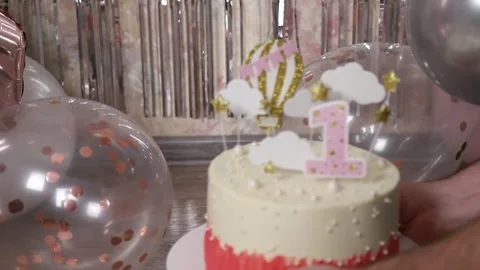 Human hands placing a cake for a first birthday on a floor with balloons Stock Footage 303359050