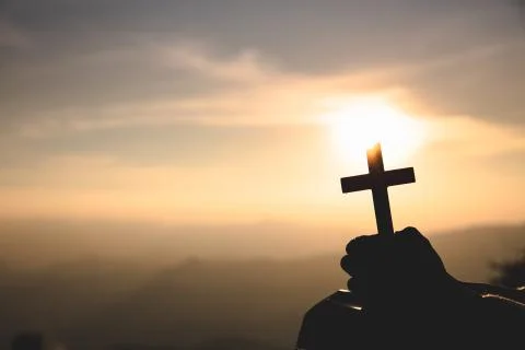 Human hands praying to the GOD while holding a crucifix symbol with bright su Stock Photos