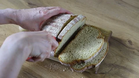 Human hands slice fresh, crisp sourdough bread on a wooden board Stock Footage 337833686