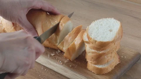Human hands slice fresh, crispy French baguette on a wooden board Stock Footage 337833666