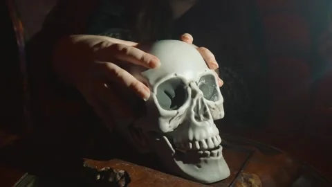 Human hands touching a mystical skull in dim light, performing a dark ritual or 스톡 동영상 321806341