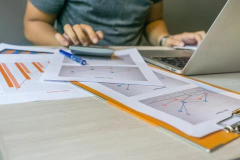 Human hands using calculator next to laptop and graph document Stock Photos