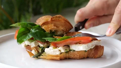 Human hands using knife and fork cut croissant with mozzarella, tomatoes, basil Stock Footage 234977624