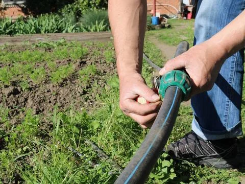 Human hands, winding on the thread of a water pipe on a green lawn Stock Photos