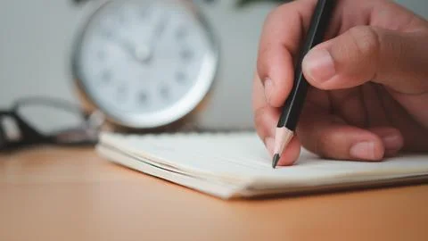 Human hands writing notes with pencil on paper on wooden table surface. Stock Photos