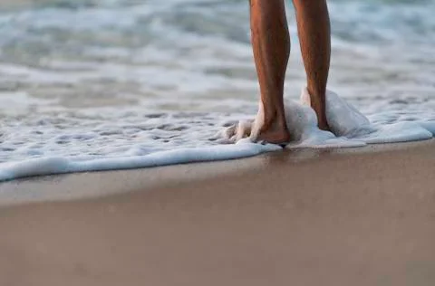 Human legs stand on beach with bubbles wave of sea Stock Photos