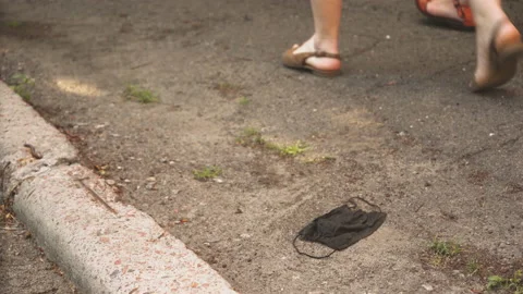 Human legs step on black face mask lying down. People walking along street Stock Footage 139445725