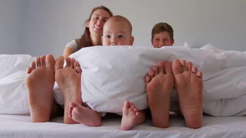 Human legs stick out from under the warm blanket. Feet of mom with children in Vidéo 151927287