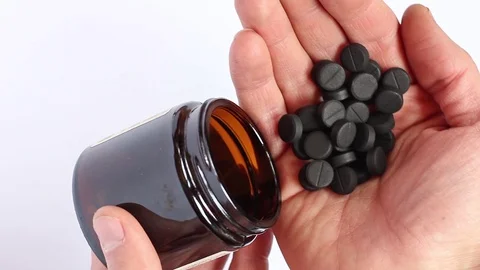 Human pours from the bottle many of black pills into the palm, top view, closeup Stockbeeldmateriaal 87066233