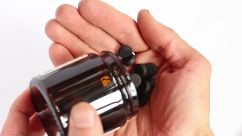 Human pours from bottle many of black pills into the palm and touches them Video stock 87066353