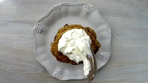 Human puts a spoon of sour cream on stack of Zucchini fritters on white plate Video stock 130066445