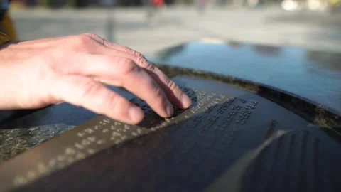 Human reads text written in Braille font sunny day street board. People on Stock Footage 178883586