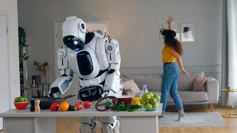 Human-like robot is cooking with a lady in VR-glasses moving near it Video stock 113015093