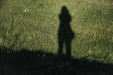 Human shadow cast across sunlit grass beside a dark foreground edge, creati.. Stock Photos