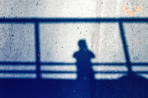 A human shadow cast on the asphalt below, seen from a pedestrian bridge. Ca.. Fotos Stock