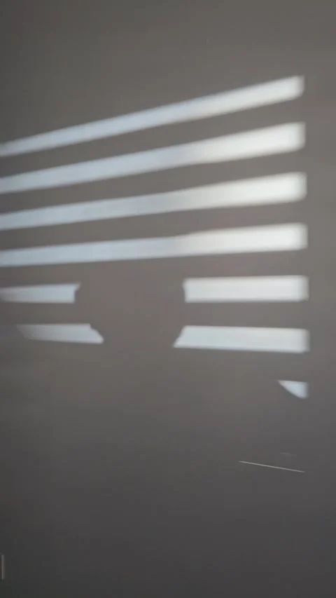 Human shadow moving across a wall crossed by bright stripes of sunlight through Видео 347778788