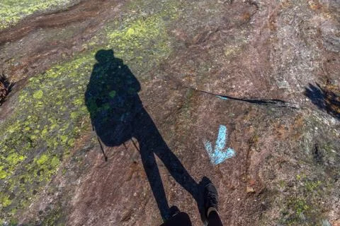Human shadow walking in wrong direction, against blue arrow on rock Stock Photos