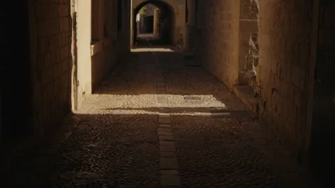 Human shadow on the wall and cobblestone alley illuminated by soft afternoon Stock Footage 313731580