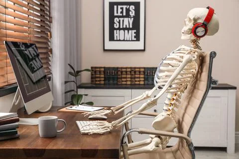 Human skeleton with headphones using computer at workplace Stock Photos