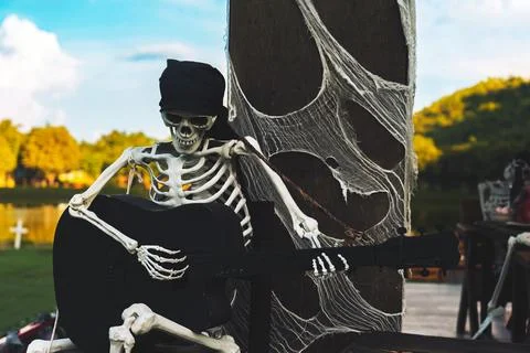 Human skeleton prop with black beanie sit on small wooden stool, holding an.. Stock Photos