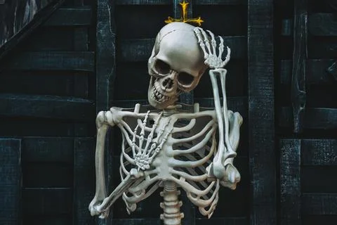 Human skeleton prop touching head against dark wooden wall and gold cross w.. Stock Photos