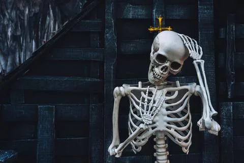 Human skeleton prop touching head against dark wooden wall and gold cross w.. Stock Photos