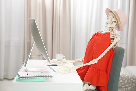 Human skeleton in red dress using computer indoors Stock Photos