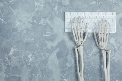 Human skeleton using computer keyboard at grey marble table, top view. Space  Stock Photos