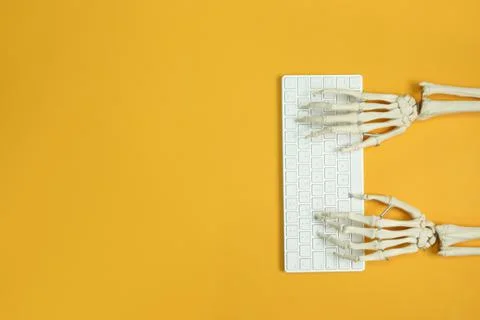 Human skeleton using computer keyboard on yellow background, top view. Space  Stock Photos