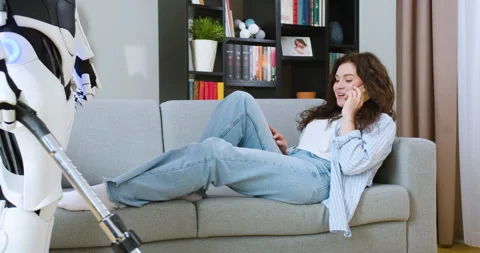Humanoid robot doing vacuum cleaning while woman with curly dark hair lying on Stock Footage 244140252