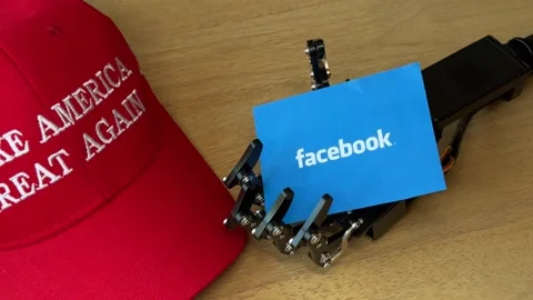 Humanoid Robot Hand Holding Facebook Card Near MAGA Hat Stock Footage 280009680