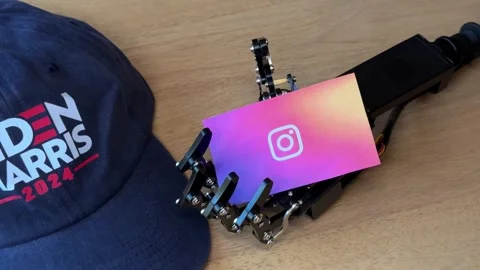 Humanoid Robot Hand Holding Instagram Card Near Biden Harris Hat Stock Footage 280009710