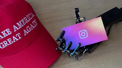 Humanoid Robot Hand Holding Instagram Card Near MAGA Hat Stock Footage 280009716
