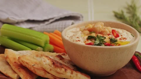 Hummus among fresh vegetables on table close-up. Hummus garnished with chickpeas Stock Footage 264422032