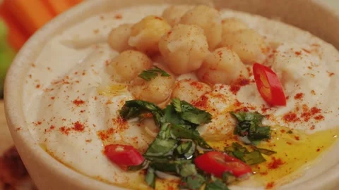 Hummus among fresh vegetables on table close-up. Hummus garnished with chickpeas Stock Footage 265163897
