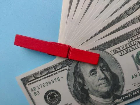 Hundred-dollar bills secured by red clothespin on blue background 스톡 사진